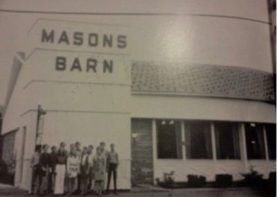 Black and white photo of a group of people standing outside a building with large letters on the front that read "MASONS BARN."